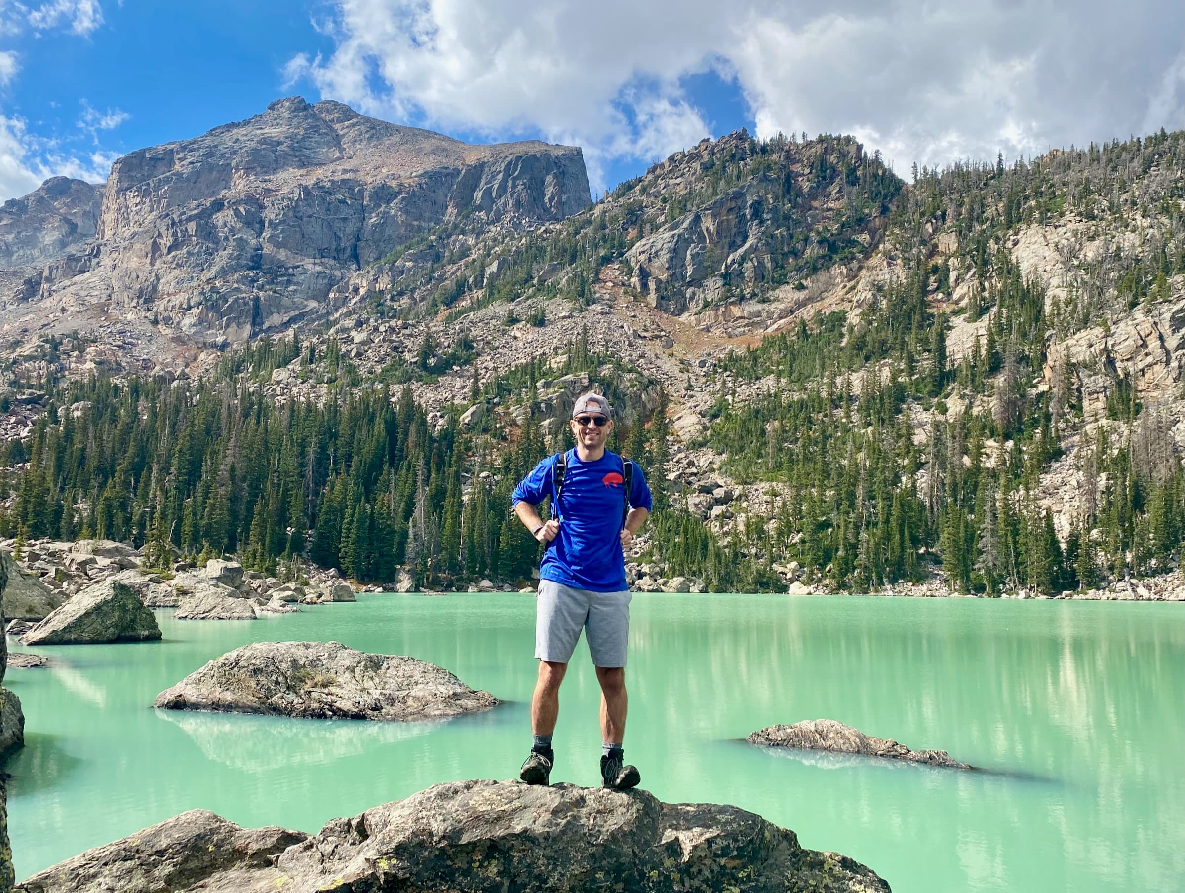 Brett standing on a boulder at a turquoise alpine lake in the Rockies