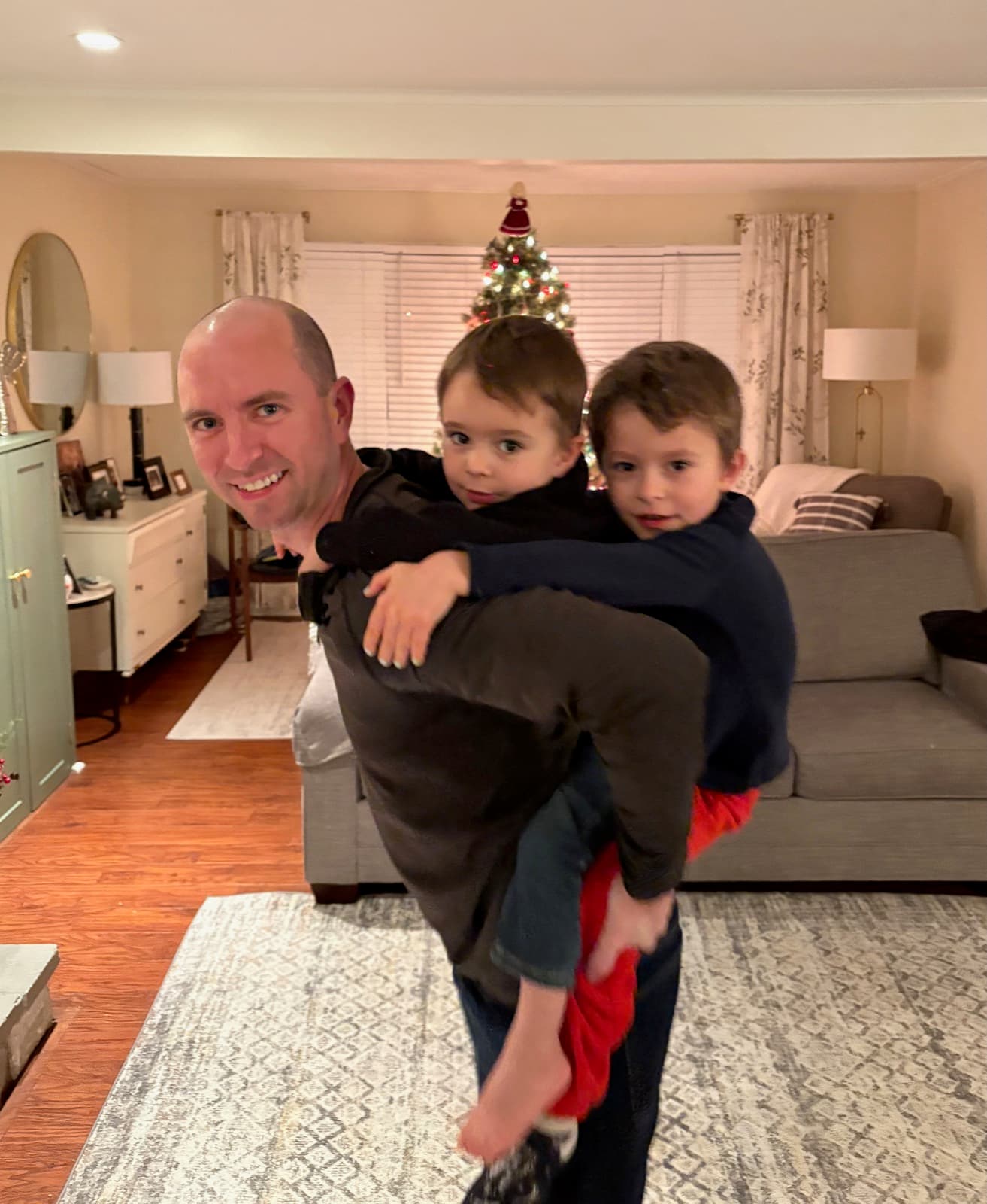 Brett carrying two young boys on his back beside a Christmas tree