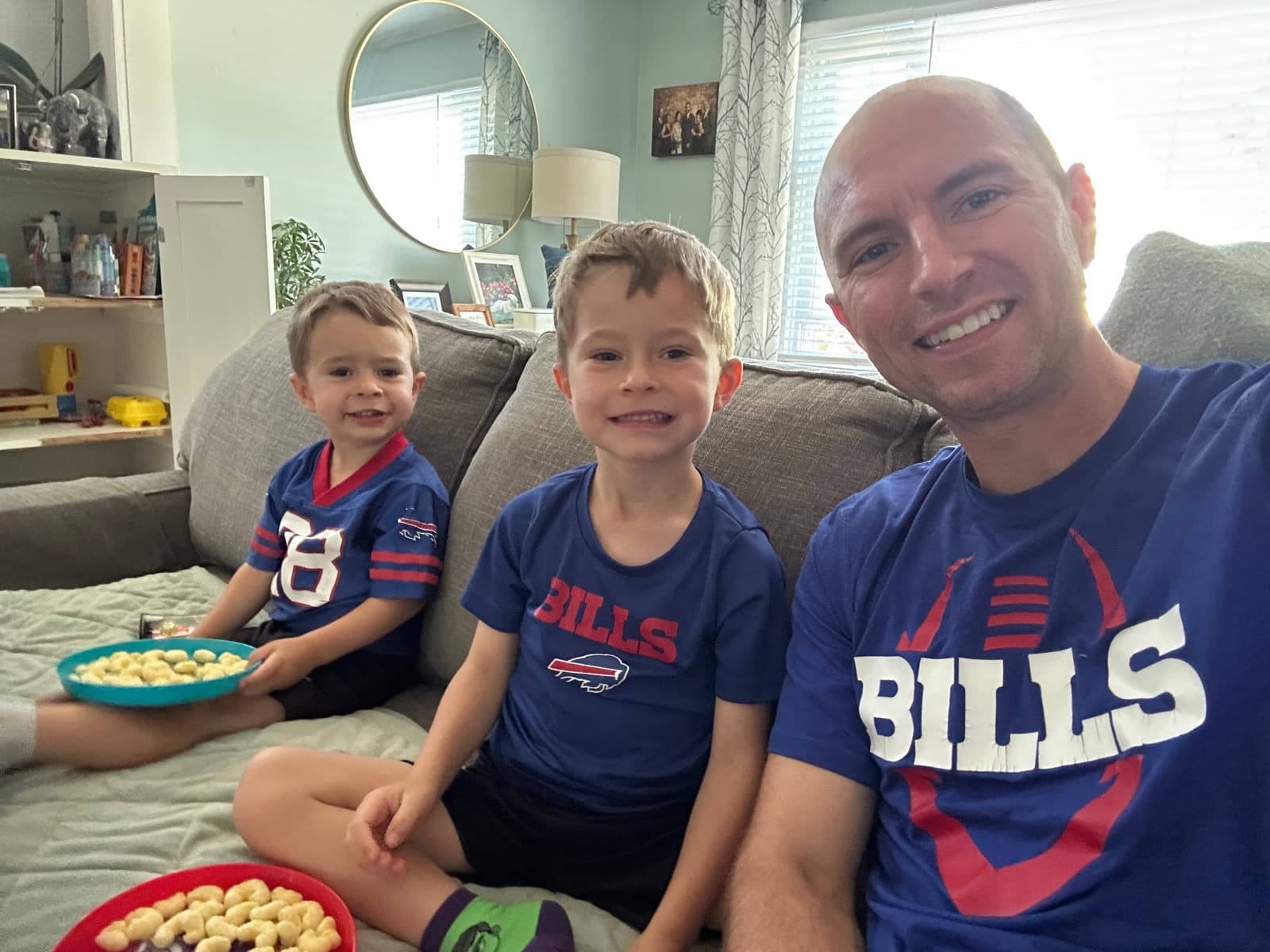 Brett and two young boys in Bills shirts watching a game at home